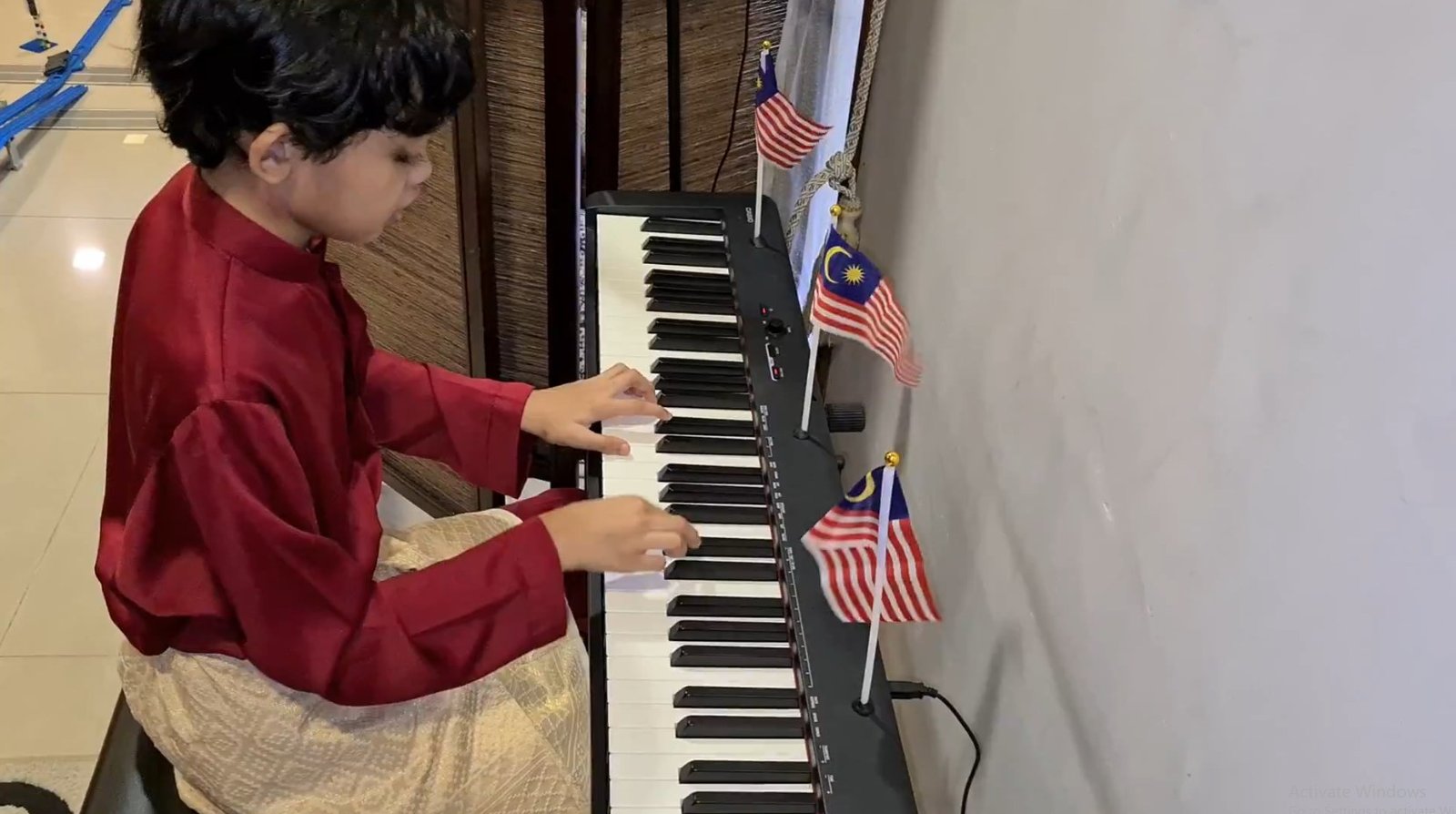 Raees Aryan Ezmir playing piano in traditional Baju Melayu attire with Malaysian flags