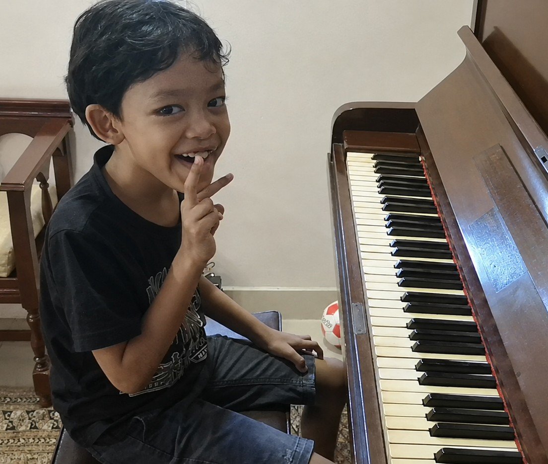 Young Raees, an autistic pianist, pointing and smiling while sitting at an old upright piano